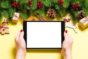 vista superior da mulher segurando o tablet nas mãos em fundo amarelo feito de decorações de natal. conceito de férias de ano novo. brincar foto