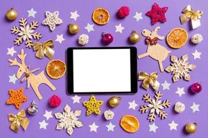 vista superior do tablet digital cercado com brinquedos de ano novo e decorações em fundo roxo. conceito de tempo de natal foto