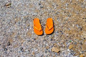 fundo de viagem com um par de chinelos laranja na areia foto