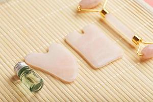 um conjunto de ferramentas para a técnica de massagem facial gua sha feita de quartzo rosa natural. rolo, pedra jade e óleo em uma jarra de vidro, em um fundo de palha para cuidados com o rosto e corpo.