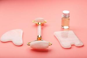 Ferramenta de massagem gua sha feita de rolo de quartzo rosa natural, pedra jade e óleo, em um fundo rosa para cuidados com o rosto e corpo. parte da medicina tradicional chinesa foto