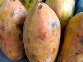 bando de mamão laranja doce. vários grandes frutos de mamão doce colocados na mesa de madeira em fundo natural para venda na loja de frutas foto