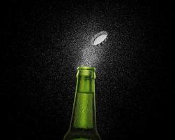 closeup foto de uma garrafa de cerveja verde espirrando gotas de cerveja em um fundo preto. tampa de cerveja voando em cima da garrafa. renderização 3D