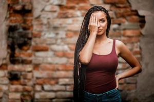 mulher com longos cabelos trançados afro posando ao ar livre contra uma parede de tijolos foto