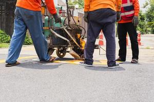 grupo de trabalhadores da estrada pintam linhas de tráfego na superfície da estrada de asfalto. foto