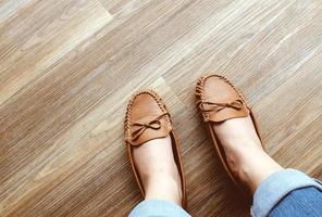 pernas de mulher em jeans usando sapatos rasos de couro no piso de madeira foto