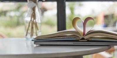 amor de livros, leitura. pilha de livros na capa colorida estava sobre a mesa. livro aberto com folhas enroladas em forma de coração. biblioteca, educação. espaço vazio para o seu texto à esquerda. foto