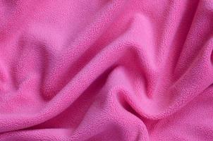 o cobertor de tecido de lã rosa peludo. um fundo de material de lã macia rosa claro com muitas dobras de relevo foto