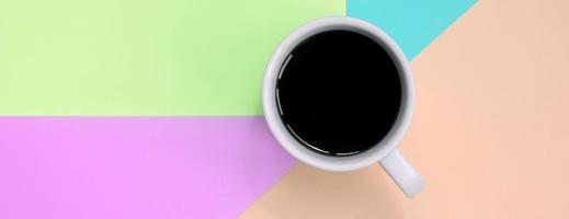 pequena xícara de café branco sobre fundo de textura de papel de cores rosa pastel, azul, coral e limão de moda foto