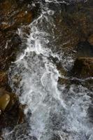 imagem aproximada de uma pequena cachoeira selvagem na forma de pequenos riachos de água entre as pedras da montanha foto