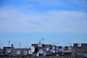 muitas antenas de televisão por satélite no telhado sob um céu azul foto