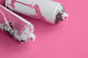 algumas latas de spray de aerossol rosa usadas com gotas de tinta estão em um cobertor de tecido de lã rosa claro macio e peludo. cor de design feminino clássico. conceito de vandalismo de graffiti foto
