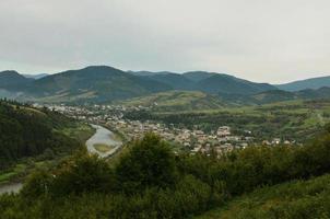 uma bela vista da vila de mezhgorye, região dos cárpatos. muitos edifícios residenciais cercados por altas montanhas da floresta e longo rio foto