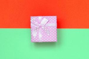 pequena caixa de presente rosa está no fundo de textura de papel de cores turquesa e vermelho pastel de moda foto