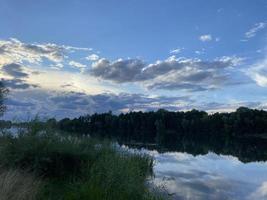 belo pôr do sol no lago. nuvens e a silhueta das árvores são refletidas na água. foto