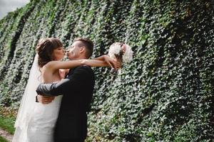 noiva e noivo no dia do casamento caminhando ao ar livre na natureza verde primavera. casal de noivos, mulher recém-casada feliz e homem abraçando no parque verde. amoroso casal de noivos ao ar livre. noiva e noivo foto