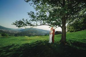 feliz elegante noiva e noivo correndo e se divertindo nas montanhas em dia ensolarado de verão. lindo casal recém-casado rindo, sentimentos verdadeiros. momento romântico emocional. foto