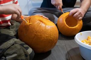 preparação do dia das bruxas. família esculpindo abóbora em jack-o-lantern enquanto está sentado no chão, em casa. foto