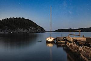 veleiro ancorado em um antigo cais, um mar calmo e um céu estrelado com a via láctea. bela paisagem noturna. foto