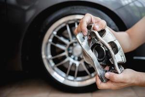 conceito de sistema de parada de corrida de serviço de carro, feche o freio de pinça do carro na mão um homem e a roda do carro em segundo plano foto