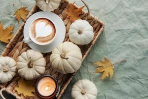 abóboras brancas, café e folhas de outono em uma bandeja de vime. foto