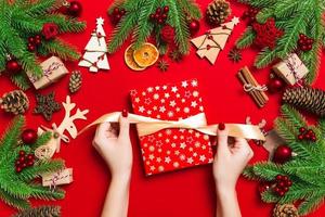 vista superior das mãos femininas segurando um presente de natal em fundo vermelho festivo. abeto e decorações de férias. conceito de feriado de ano novo foto
