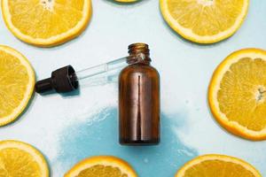 frasco de vidro marrom com um soro de pipeta com vitamina c. óleo essencial e fatias de laranja. conceito de saúde e beleza. foto