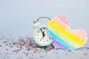 despertador mostrando cinco minutos a doze com lantejoulas multicoloridas e bandeira lgtb em forma de coração foto