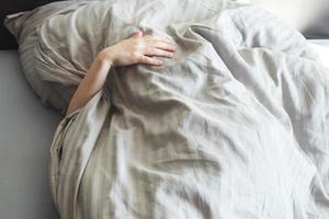 menino dorme na cama. criança deita-se no travesseiro e cobre o rosto com um cobertor foto