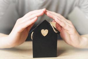 casinha de brinquedo coberta de mão da mulher. conceito de seguro residencial foto