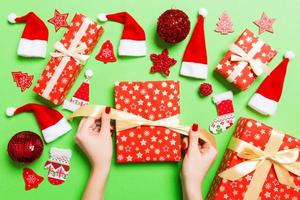 vista superior das mãos femininas segurando um presente de natal em fundo verde festivo. chapéus de papai noel e decorações de férias. conceito de feriado de ano novo foto