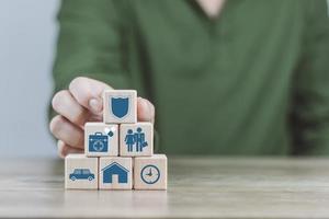 conceito de seguro, a mão de um homem está construindo um cubo de madeira para mostrar a decisão sobre o seguro de vida para planejar o futuro para si e suas famílias em dinheiro, saúde e incentivos fiscais. foto