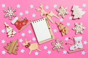 vista superior do notebook, fundo rosa decorado com brinquedos festivos e renas de símbolos de natal e árvores de ano novo. conceito de férias foto