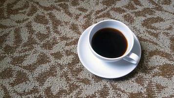 vista superior da xícara branca de café preto no tapete marrom ou fundo do tapete com espaço de cópia. postura plana de bebida quente no papel de parede de algodão. foto