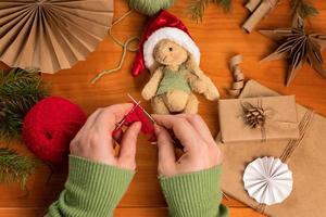 mãos femininas tricotando um cachecol para um coelhinho de brinquedo feito na técnica de pelúcia. brinquedo feito à mão e roupas para ele. foto