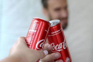carcóvia. ucrânia - 2 de maio de 2022 jovem feliz levanta lata de coca-cola com amiga no interior da garagem foto