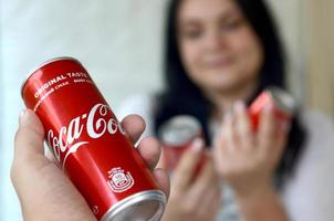 carcóvia. ucrânia - 2 de maio de 2022 mulher feliz segurando algumas latas de coca-cola no interior da garagem e mão masculina com uma lata em primeiro plano foto