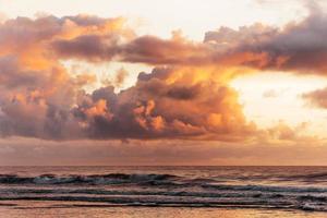 nuvens fofas do pôr do sol acima das ondas foto