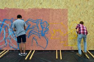 carcóvia. ucrânia - 2 de maio de 2022 festival de artes de rua. jovens desenham grafite em paredes de madeira portáteis no centro da cidade. o processo de pintura em paredes com latas de aerossol foto