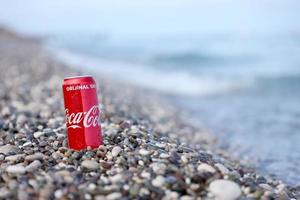 antalya, turquia - 18 de maio de 2022 lata vermelha original da coca cola encontra-se em pequenas pedras redondas perto da costa do mar. coca-cola na praia turca foto