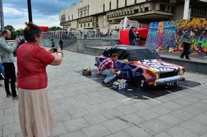 carcóvia. ucrânia - 2 de maio de 2022 festival de arte de rua. jovens desenham grafite na carroceria do carro no centro da cidade. o processo de desenhar graffiti colorido em um carro com latas de aerossol foto