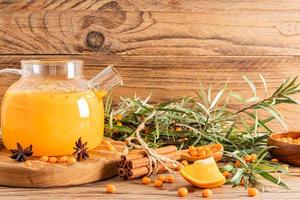 chá de espinheiro mar quente com canela, laranja, anis em um bule de vidro em uma placa de madeira e mesa. o conceito de curar o corpo em clima frio.