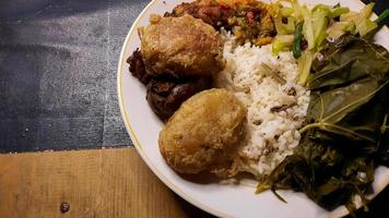 ângulo superior, menu warteg comida tradicional indonésia, com bolos de batata e folhas frescas de mandioca 02 foto