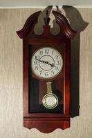 relógio de parede de madeira marrom em casa com um pêndulo em uma parede leve foto