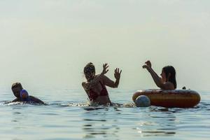 mãe e filhos nadam no mar, jogam água e se divertem, férias na praia foto