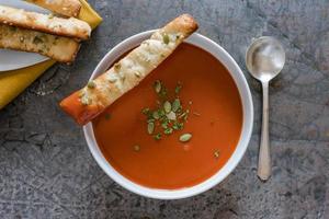 sopa de tomate em uma tigela com palitos de pão foto