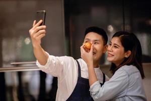 um casal sorridente de homens e mulheres usando telefone na cozinha. tirando selfie ou transmissão ao vivo via smartphone enquanto prepara uma comida vegana. conceito moderno de estilo de vida saudável. cozinhando em casa juntos foto