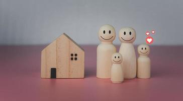 conceito de casa feliz. casa modelo com bonecos de madeira em pé alinhados em fundo rosa e ícones de coração. indica felicidade e amor no lar. foto