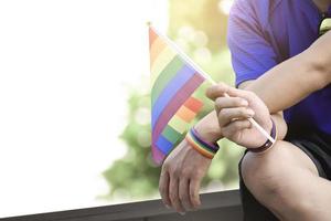 bandeira do arco-íris na mão de gay asiático que usa pulseira de arco-íris para chamar e mostra a diversidade de gênero lgbt e respeitando a alternativa de gênero em todo o mundo. foto