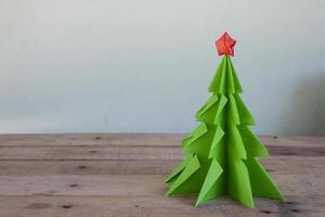 conceito origami o papel na árvore de natal e estrela vermelha na mesa de madeira marrom. foto